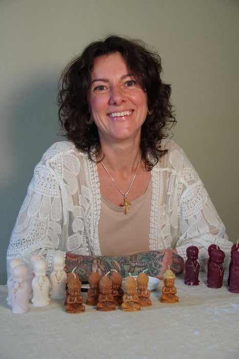 Nadja ist ein Mitglied der Klostergemeinschaft Gut Saunstorf. Sie sitzt an einem Tisch und vor ihr stehen verschiedene Buddha-Kerzen, die sie in liebevoller Handarbeit gegossen hat.
Dafür nutzt sie Kerzenwachsreste, die im Kloster gesammelt und wiederverwendet werden.