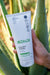 "Aloe Vera Körperpeeling" in Tube aus Kunststoff vor einer Aloe Vera Pflanze.
